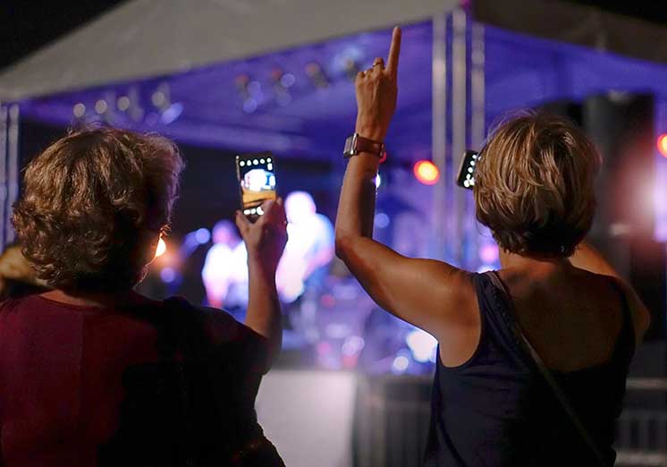Image show two woman taking picture with phone at a concert