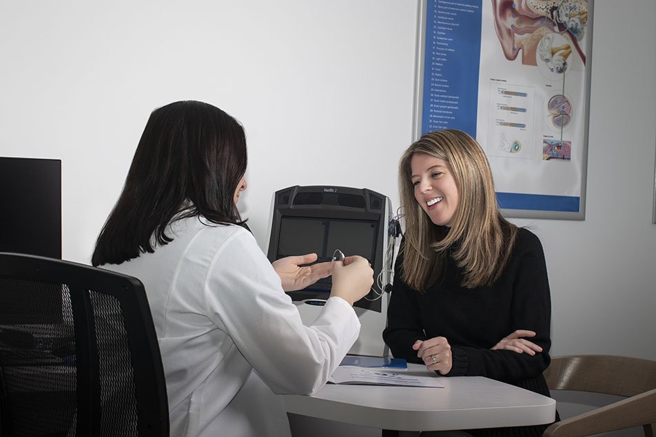 Image shows audiologist and woman in a hearing clinic laughing 