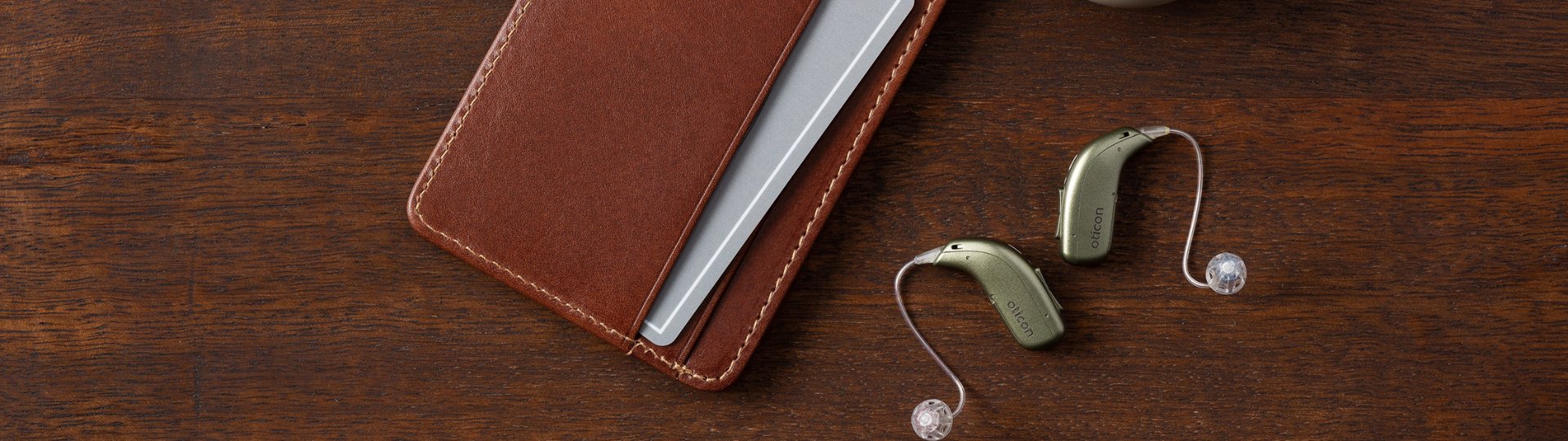 a pair of hearing aids with a wallet on a dark wood background