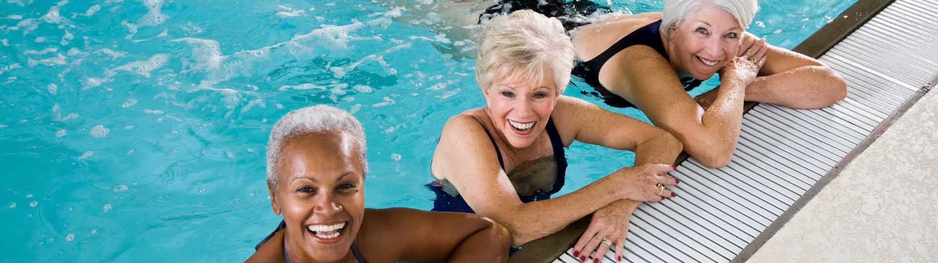 three women in a pool smiling up at the camera