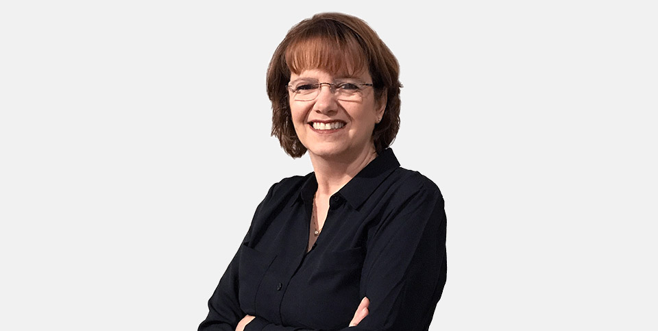 Woman smiling, arms crossed, wearing glasses and a black shirt, posed against a plain white background.