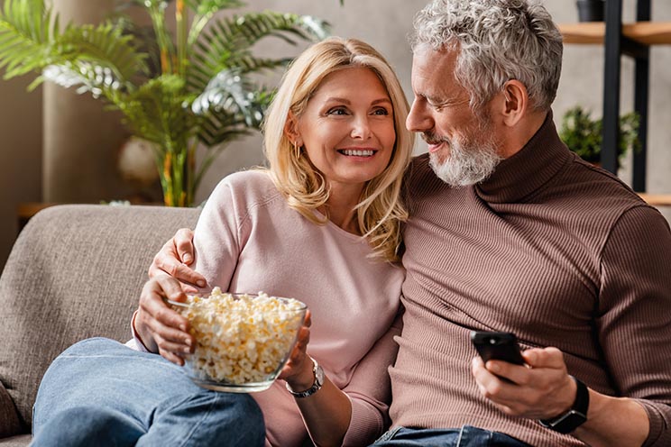Image show couple in sofa watching tv and eating popcorn