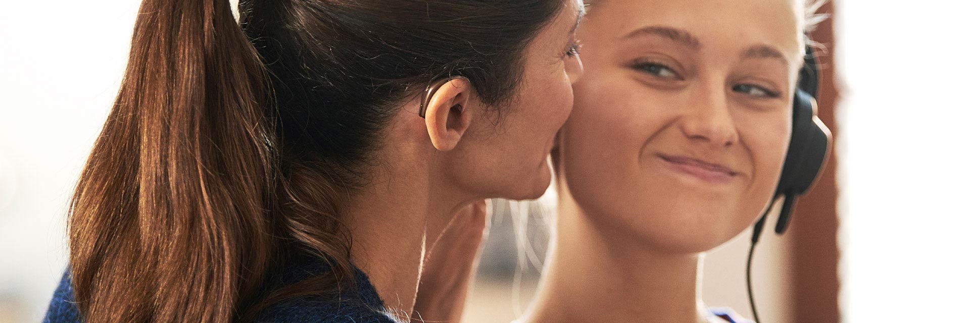Image shows woman with hearing aid in her ear and girl smiling at each other 