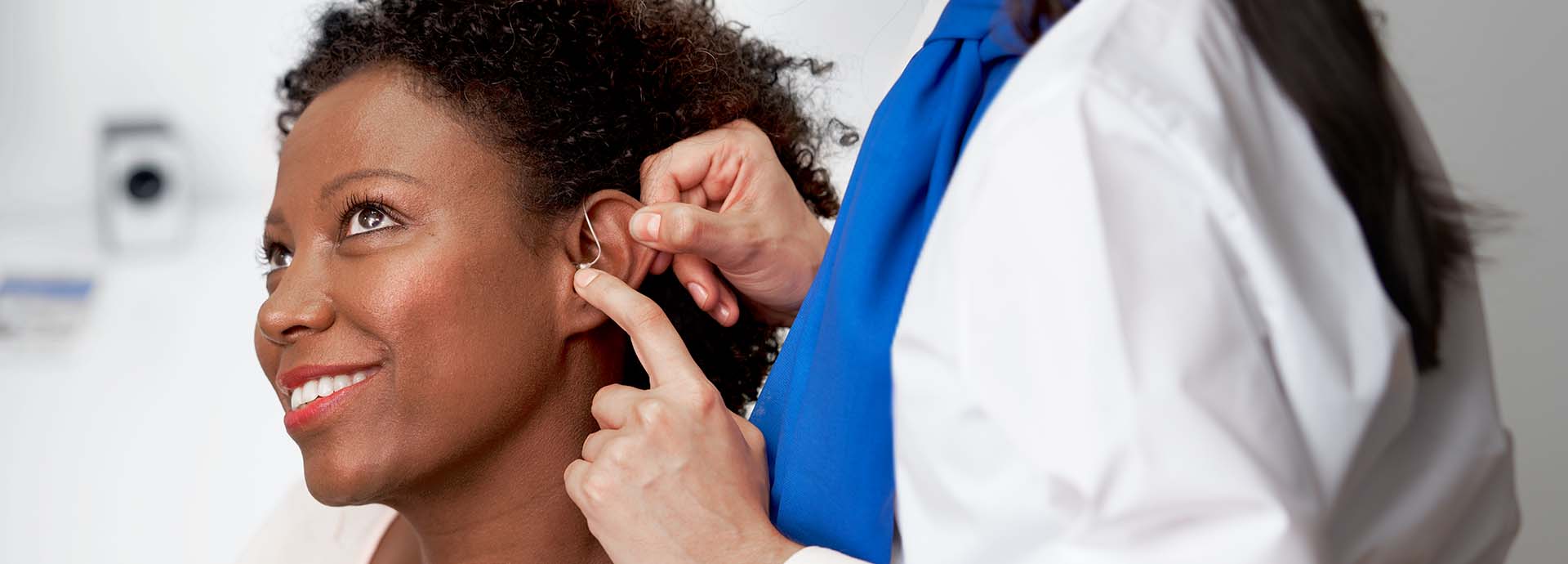 Image shows woman having a hearing aid placed behind her ear