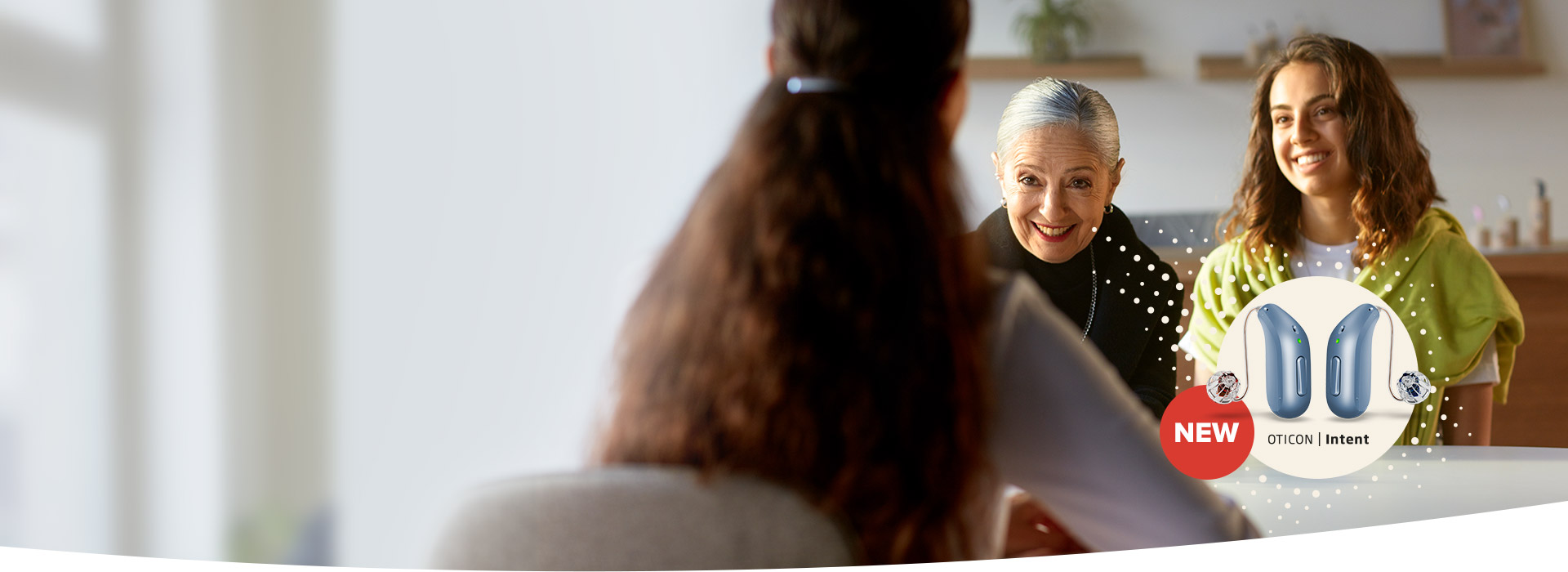 An elderly woman and a younger woman smile at someone in a home setting, with a hearing aid advertisement for 