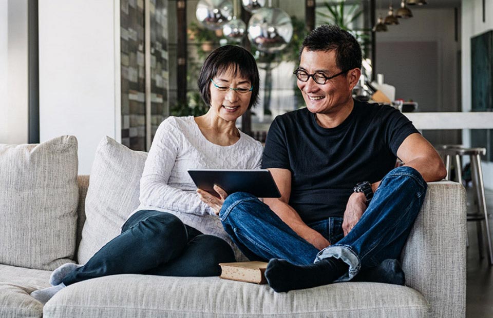 Image shows couple sitting on the sofa looking at a tablet