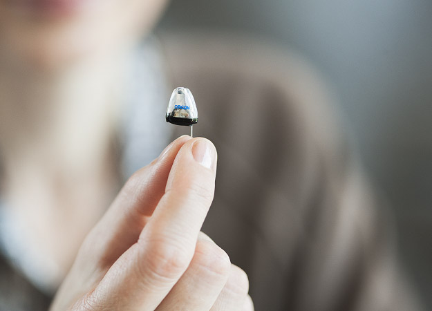 Image shows a hand holding an invisible hearing aid. 