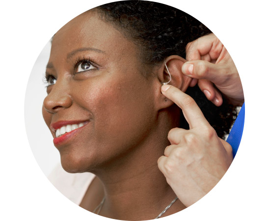 Image shows woman having a hearing aid placed behind her ear